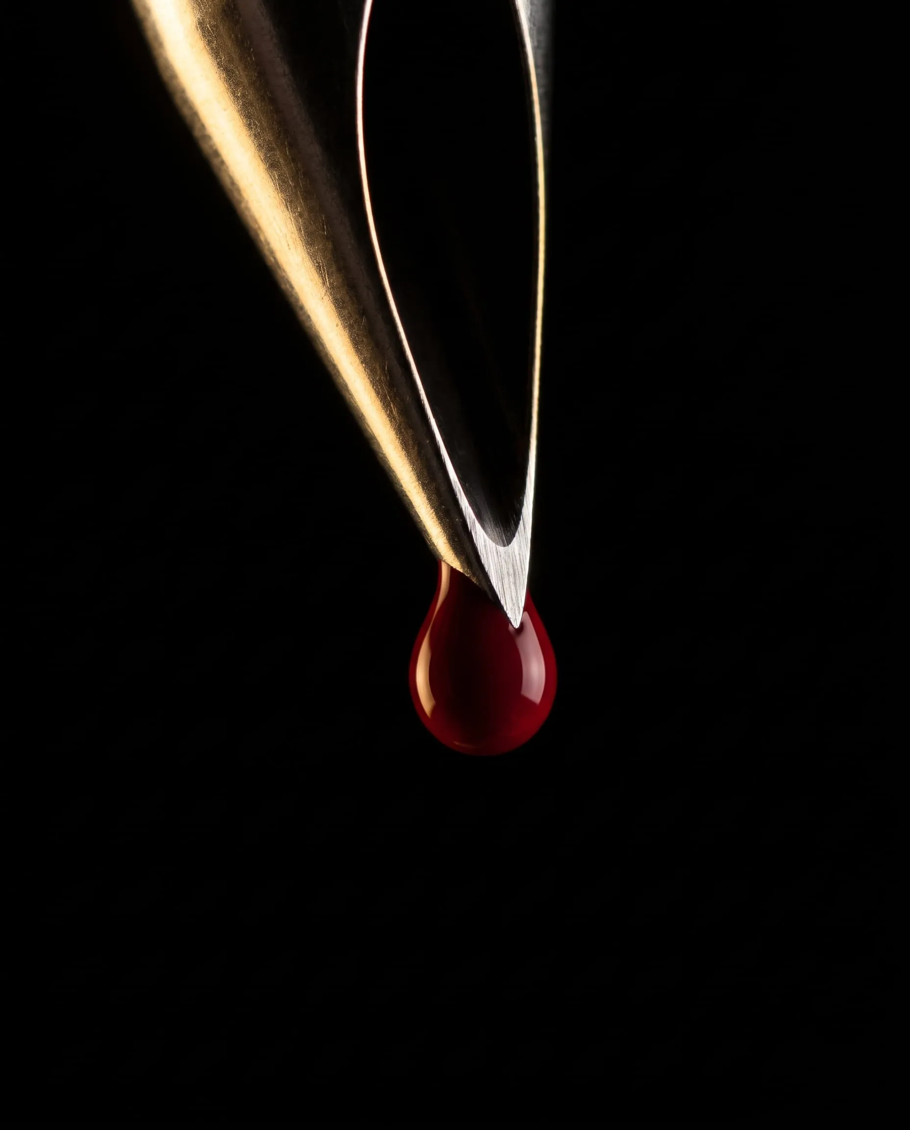 The tip of a tattoo needle holding a single drop of red ink