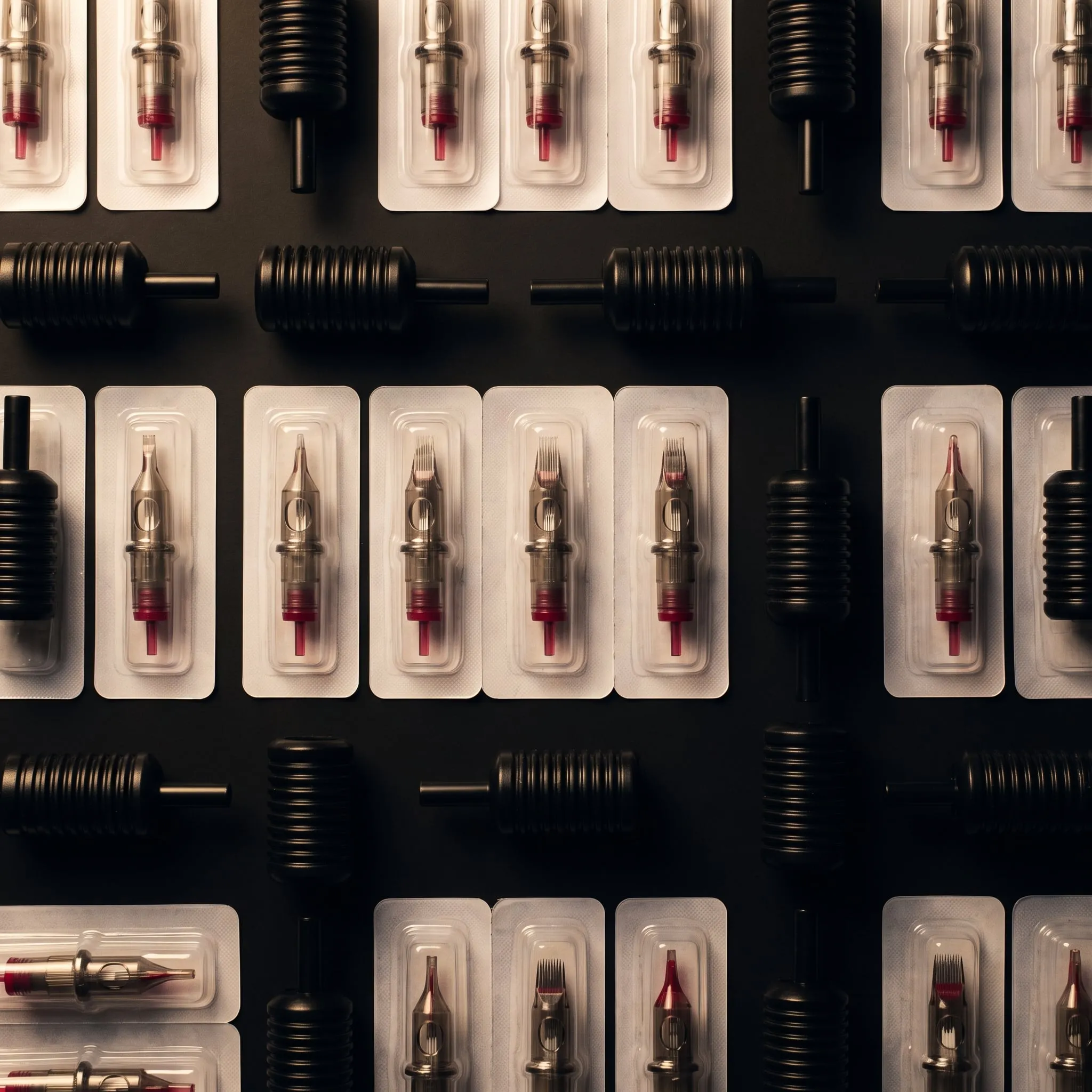 Sealed needle cartridges and black disposable grips laid out in rows