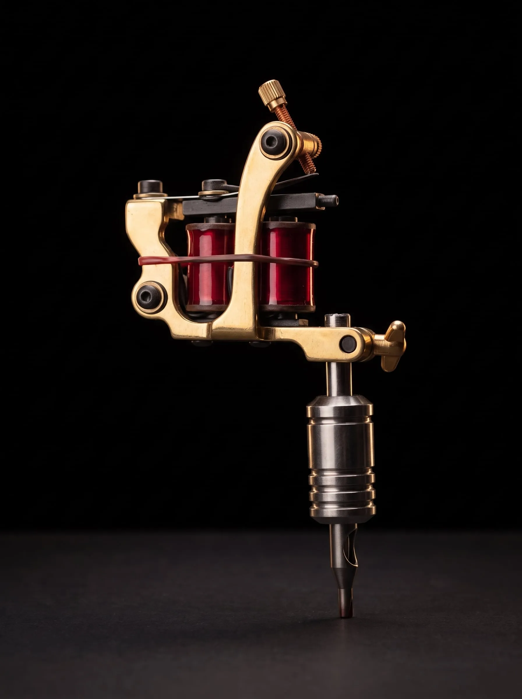 A brass coil tattoo machine with red coils standing upright on black